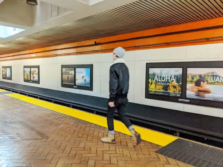 A commuter walks past Aloha and Luana ads in an OAK takeover of a BART station